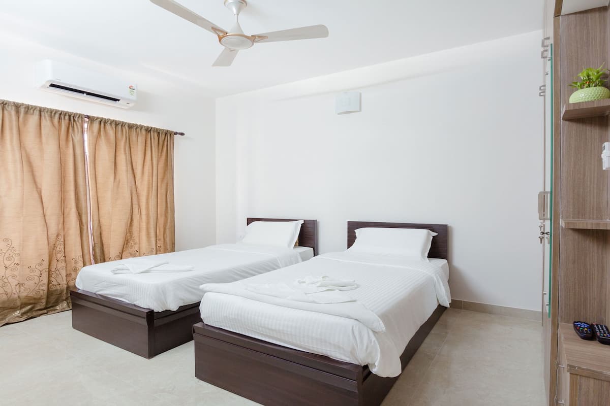Quarto de hotel com duas camas, um ventilador de teto, um aparelho de ar condicionado, um guarda-roupa e um controle remoto sobre o guarda-roupa.