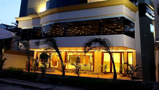 A multi-story hotel with a modern design, featuring a curved facade and a ground-level entrance with a reception area. - Aroma Classic Days (Thiruvananthapuram)