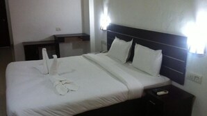 A neatly made bed with white linens and pillows, a bedside table with a remote control, and a wall-mounted light fixture. - Aroma Classic Days (Thiruvananthapuram)