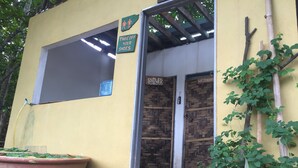 A building entrance with a sign instructing to take off shoes, a shower area, and a large planter with plants. - Bakau Hijau Riverlodge - Hostel (Bedung)
