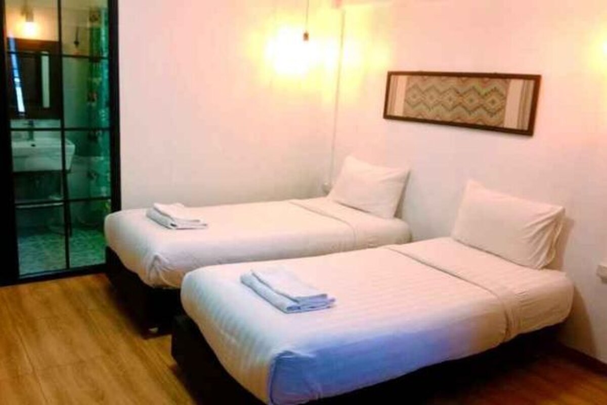 A hotel room with two beds, a glass door leading to a bathroom, and a framed picture on the wall.
