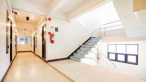 A clean, well-lit hallway leading to a staircase with a glass railing, fire safety equipment, and a window.