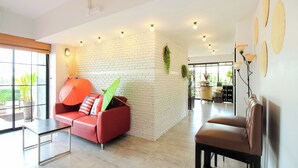 A spacious living area with a red sofa, a coffee table, and a brown chair. There is a white brick wall and a large window providing natural light.