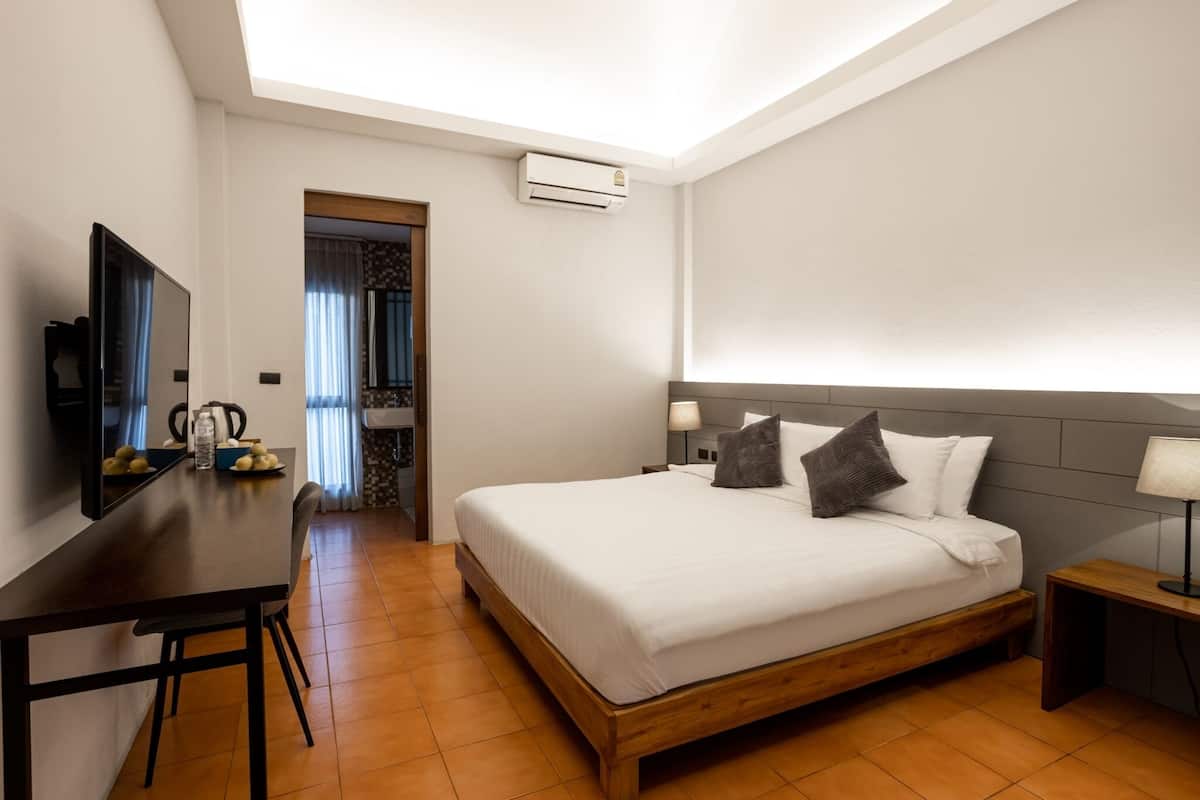 A modern hotel room with a wooden bed, a desk with a flat-screen TV, and a small table with a kettle.