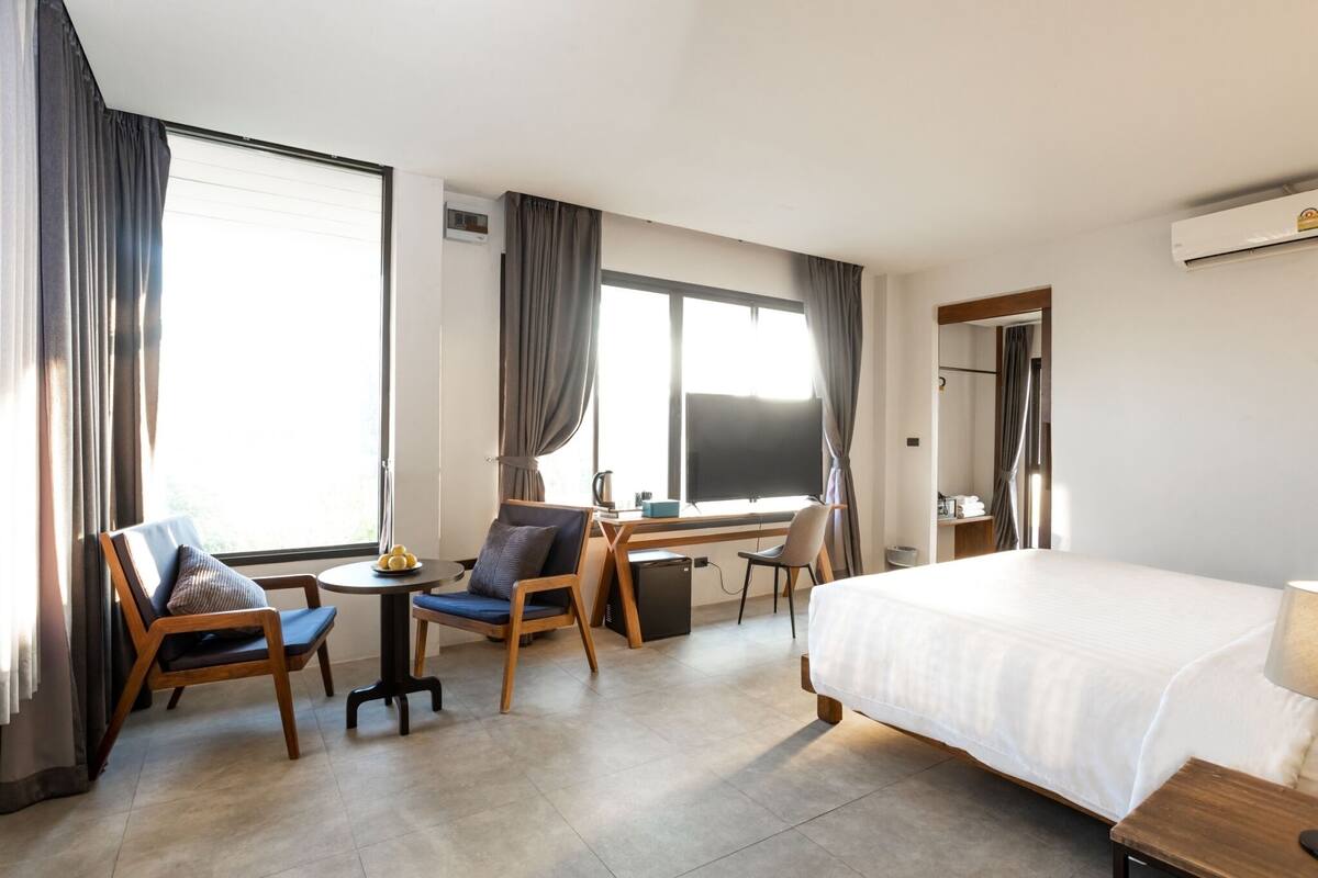 A hotel room with a bed, a desk, two chairs, a small table, and a window with curtains.