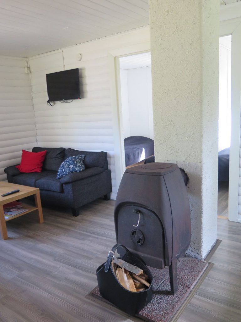A living room with a sofa, a television mounted on the wall, and a wood-burning stove.