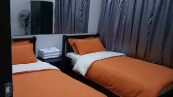 A hotel room with two single beds, a bedside table, a mirror, a fan, and curtains.