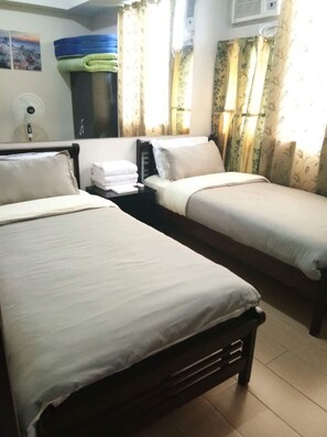 Une chambre d’hôtel avec deux lits simples, une table de chevet avec une lampe et une fenêtre avec des rideaux.