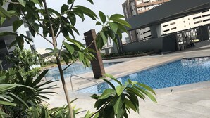 A swimming pool surrounded by greenery and modern buildings. - Cubao ManhattanHeights Unit 4Q Tower D (Quezon City)