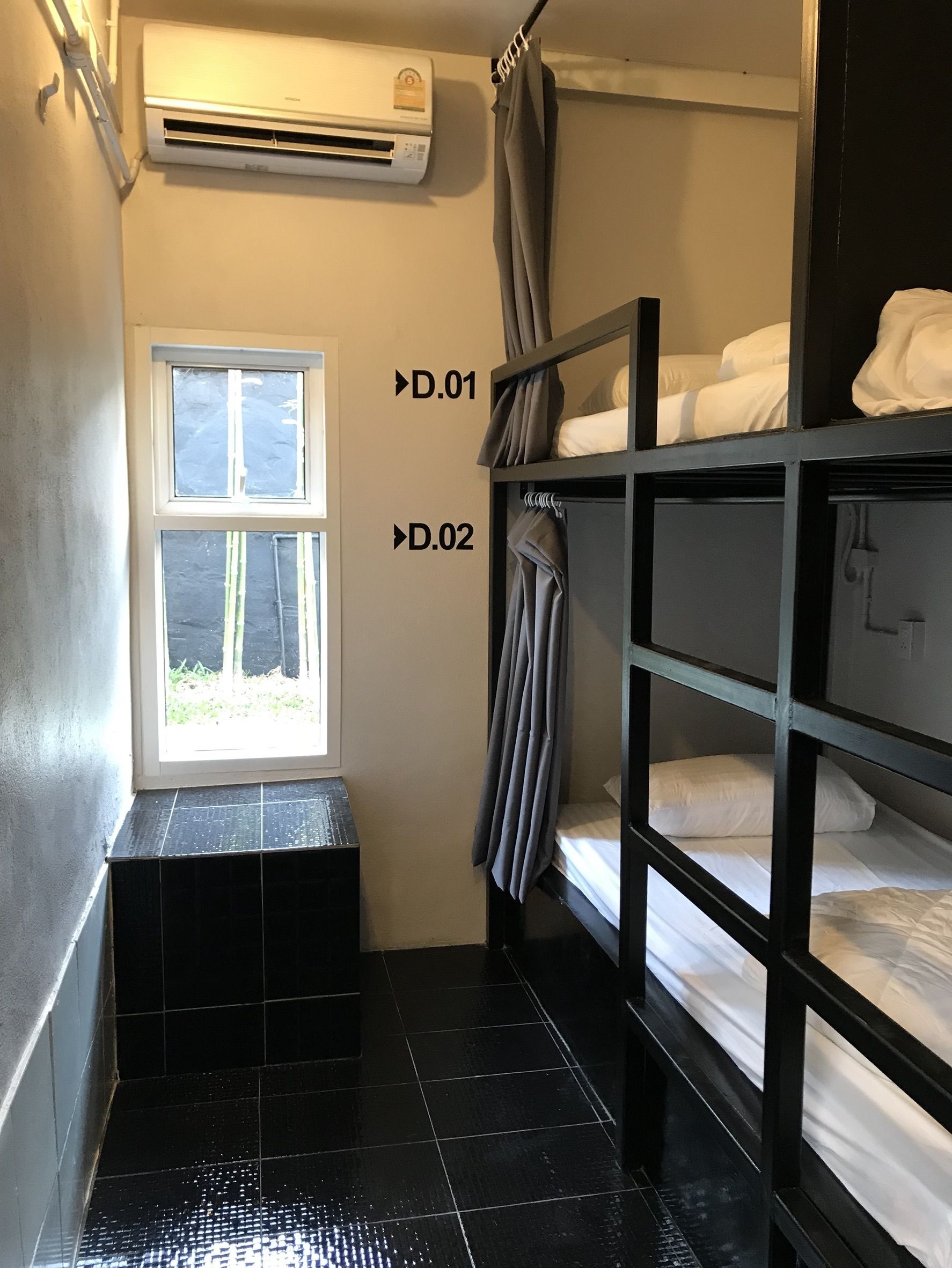 Une petite chambre avec des lits superposés, une fenêtre et un appareil de climatisation.