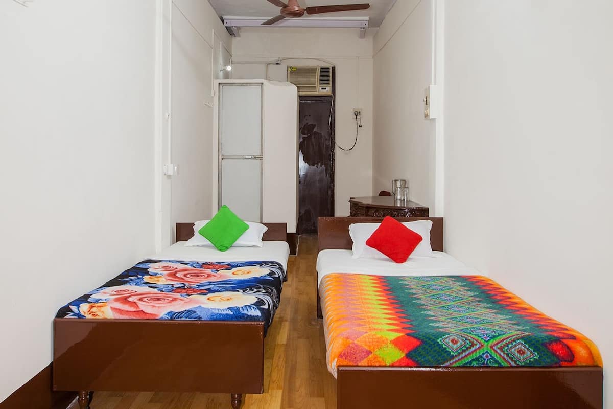 A narrow hallway with two single beds, each with colorful bedding and a pillow. A ceiling fan is visible in the center.