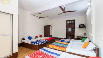A hotel room with three beds, a wardrobe, a desk with a television, and ceiling fans.