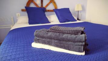 A neatly made bed with a blue quilt and pillows, a wooden headboard, and a lamp on the side.