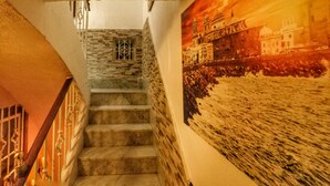 Een trap met stenen treden en een metalen leuning, die leidt naar een kamer met een groot muurdecoratie waarop een historisch gebouw en rivier te zien zijn.
