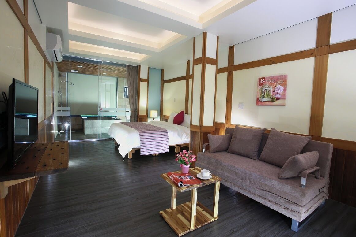 A hotel room with a bed, a sofa, a TV, a small table with a flower vase, and a painting on the wall.