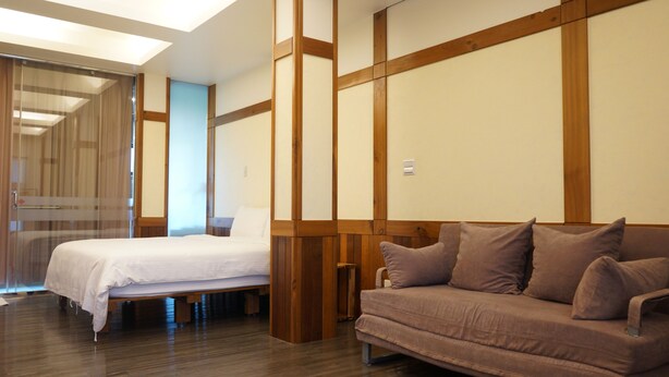 A hotel room with a bed, a sofa, wooden paneling, and a sliding door. - Artisan B&B (Toucheng)