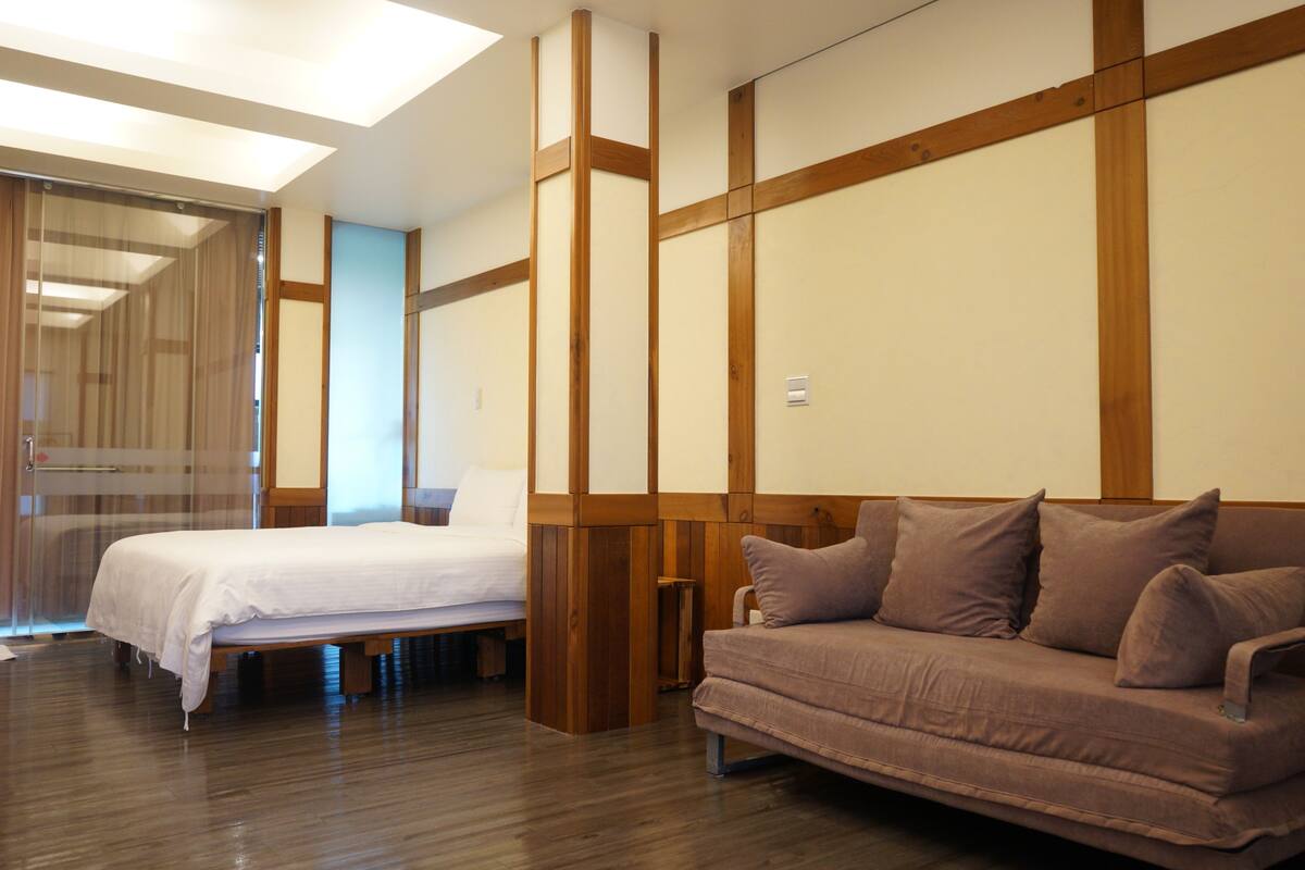 Una habitación de hotel con cama, sofá, paneles de madera y una puerta corredera.