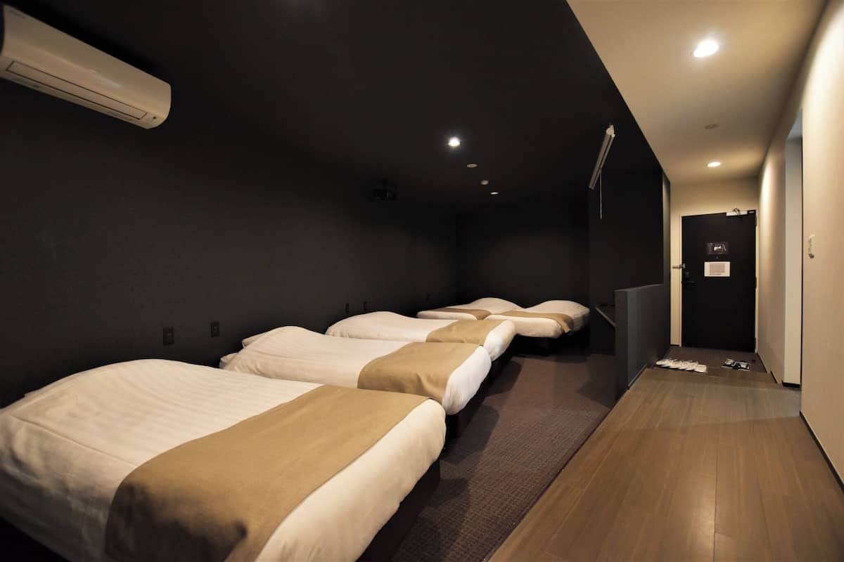A hotel room with four beds aligned in a row, a dark wall, and a wooden floor.