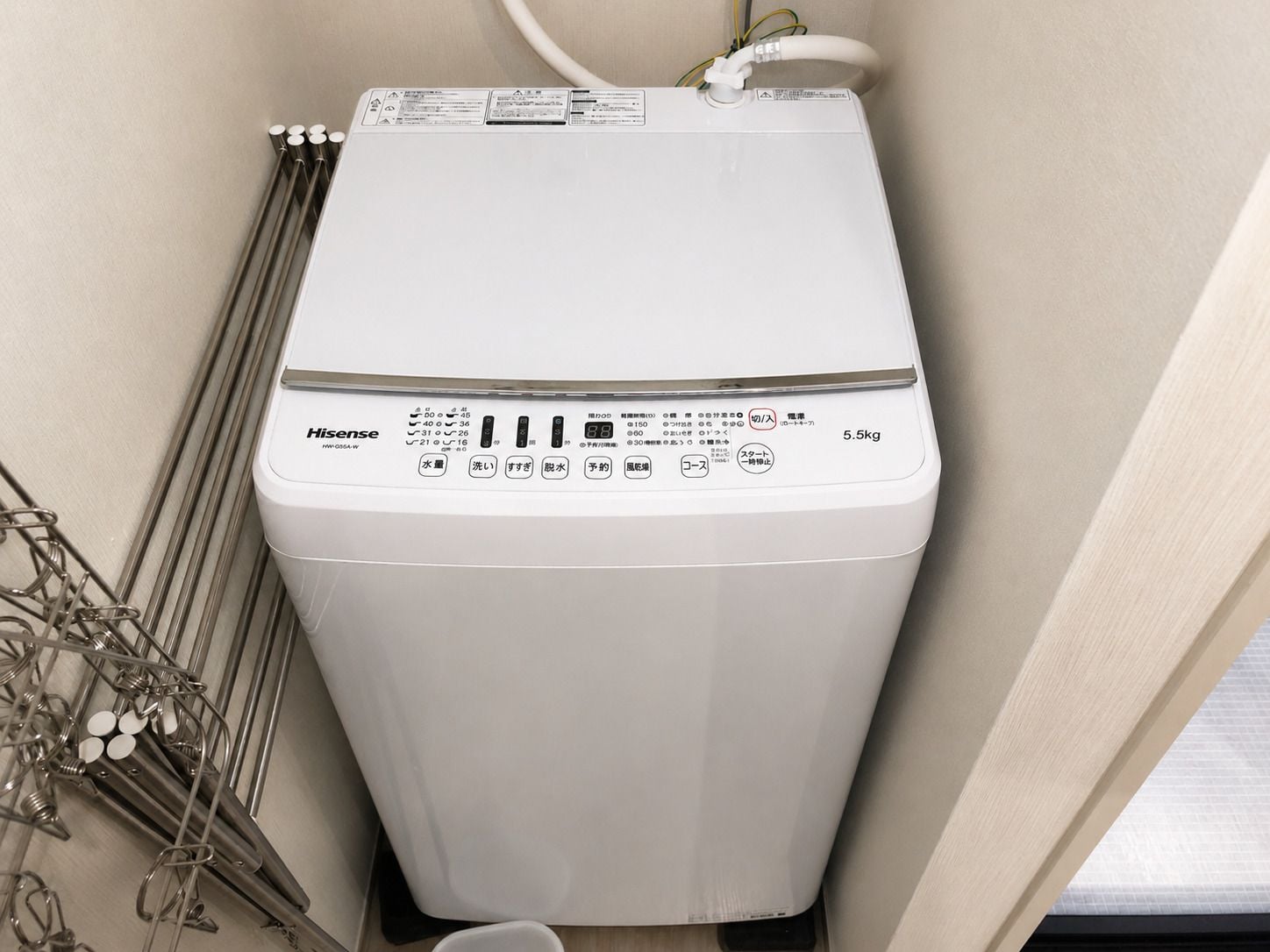 A compact, white, wall-mounted heater with multiple control buttons and a digital display, situated in a corner with a metal rack nearby.
