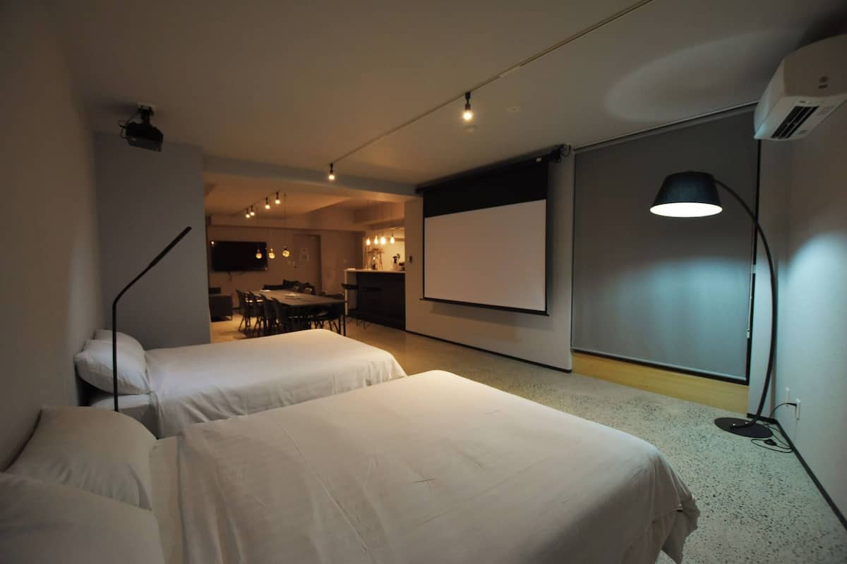 A hotel room with two beds, a projector screen, a desk, and a dining area.