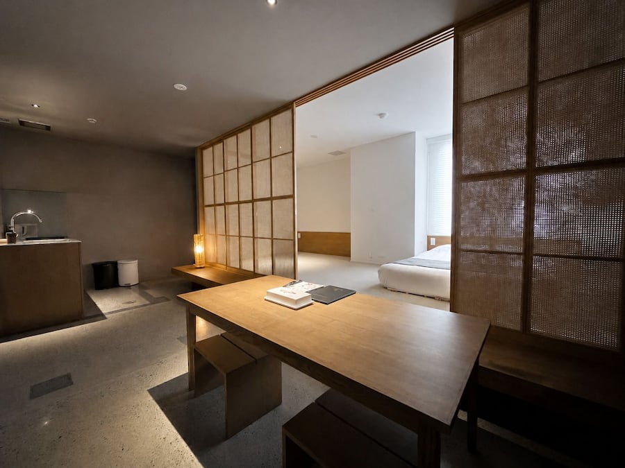 Quarto de hotel moderno com escrivaninha de madeira, mesa de cabeceira, um espelho grande e uma cama.