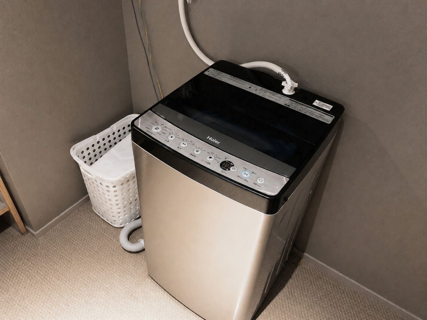 A compact, stainless steel front-loading washer and dryer unit with a control panel, a white laundry basket, and a hose.