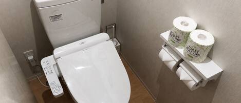 A modern toilet with a control panel, a toilet paper holder with two rolls, and a power outlet on the wall.