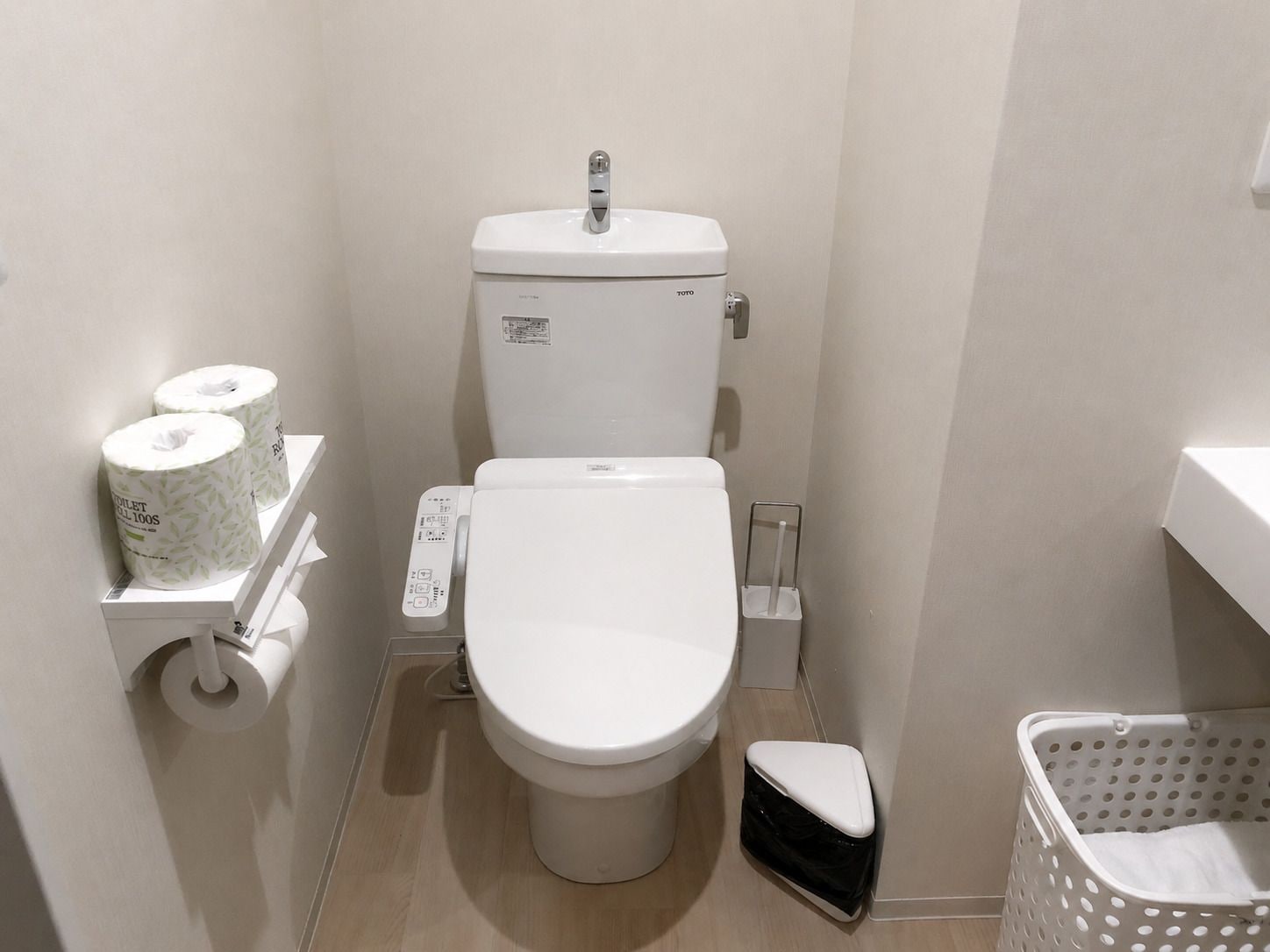 A small, compact bathroom with a toilet, a toilet paper holder, a bidet, and a laundry basket.