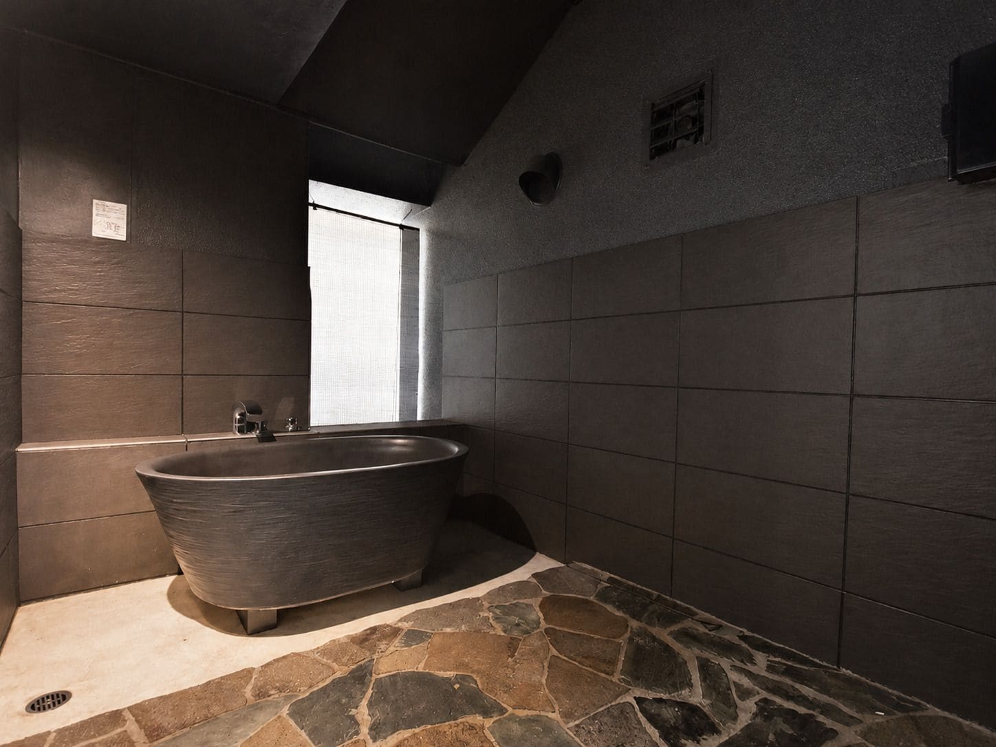 Un baño moderno con una bañera independiente, suelo de piedra y una ventana que proporciona luz natural.