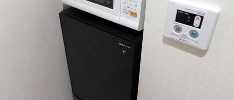 A black refrigerator with a Panasonic microwave on top, and a control panel on the wall.