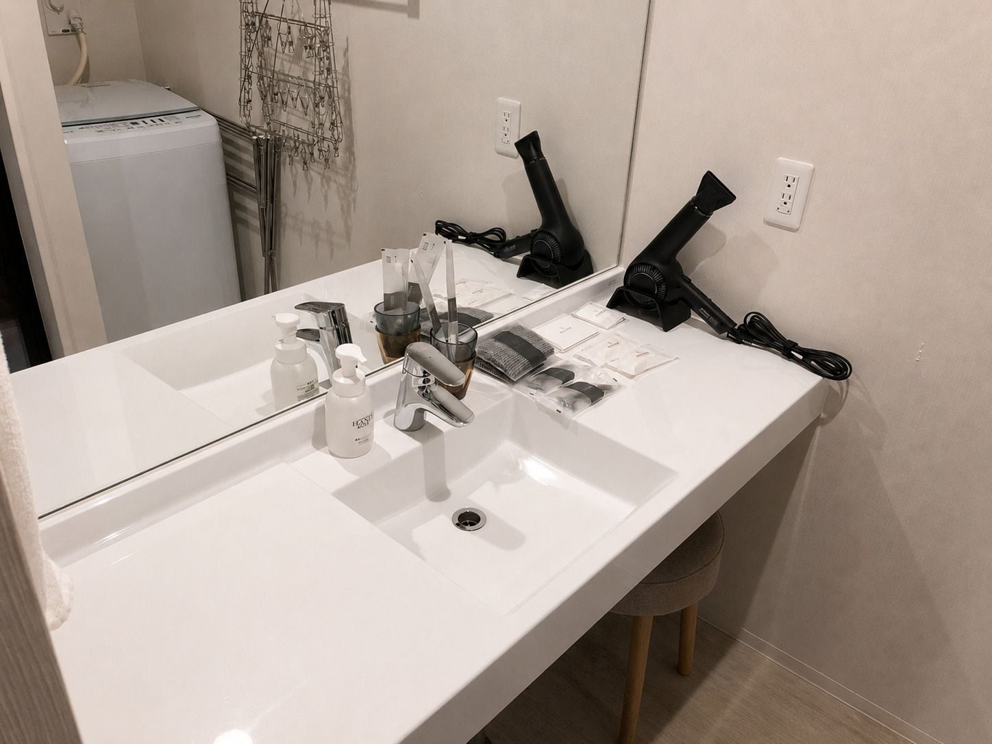 Un baño con lavamanos blanco, espejo, secador de pelo y artículos de aseo.