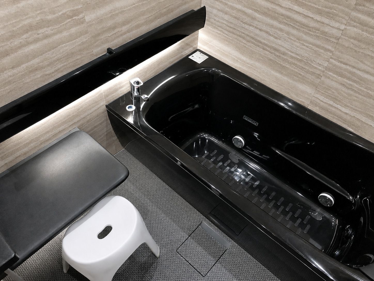 Une salle de bain moderne avec une baignoire noire, un tabouret blanc et un banc noir.