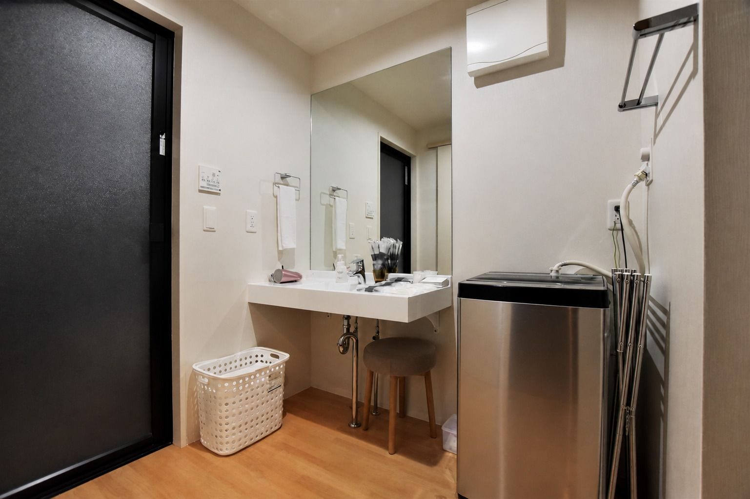 A compact bathroom with a white sink, mirror, and stainless steel shower. A white laundry basket is on the floor.