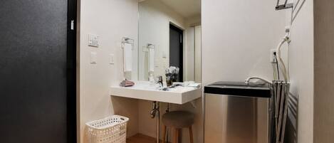 A compact bathroom with a white sink, mirror, and stainless steel shower. A white laundry basket is on the floor.