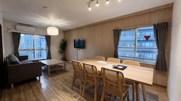 Una sala de estar moderna con un sofá, una mesa de comedor con sillas, un televisor y ventanas amplias con cortinas.