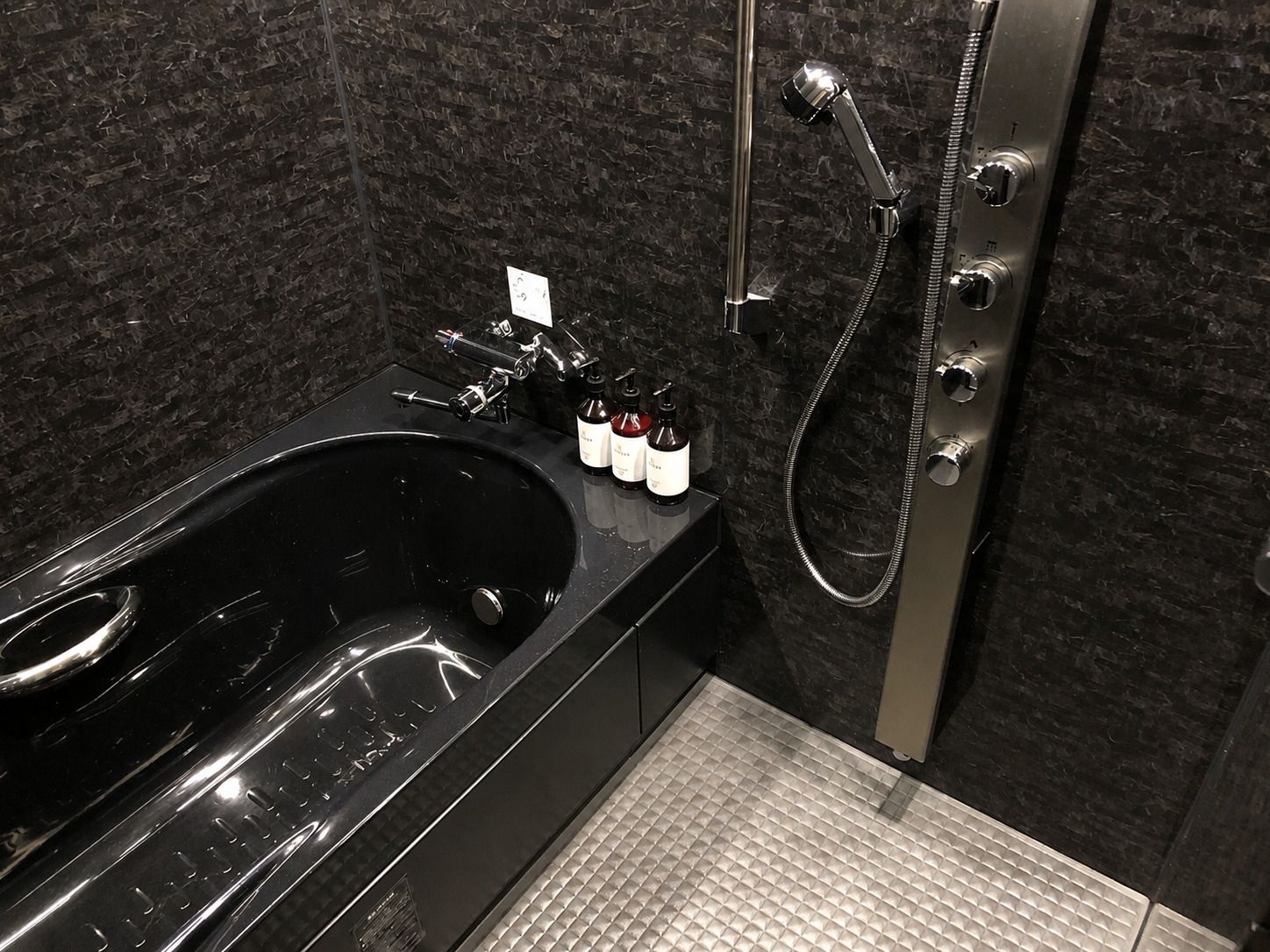 A modern bathroom with a black bathtub, a handheld showerhead, and a set of toiletries on the counter.