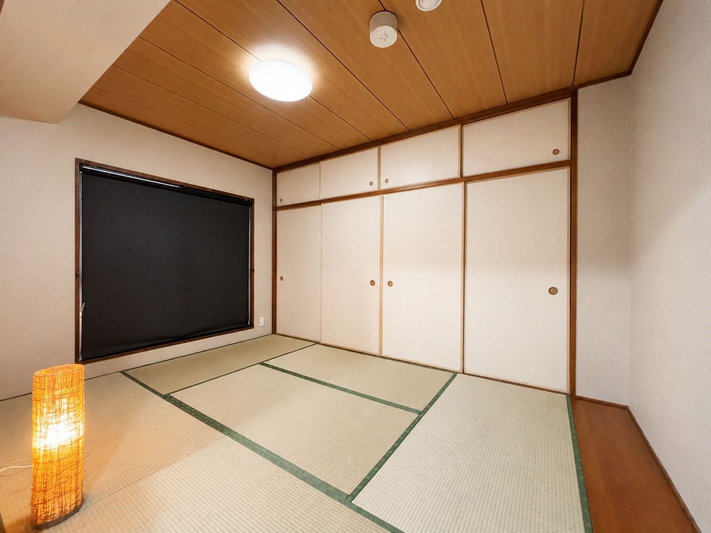 A traditional Japanese room with tatami flooring, a sliding door, and a low ceiling with recessed lighting.