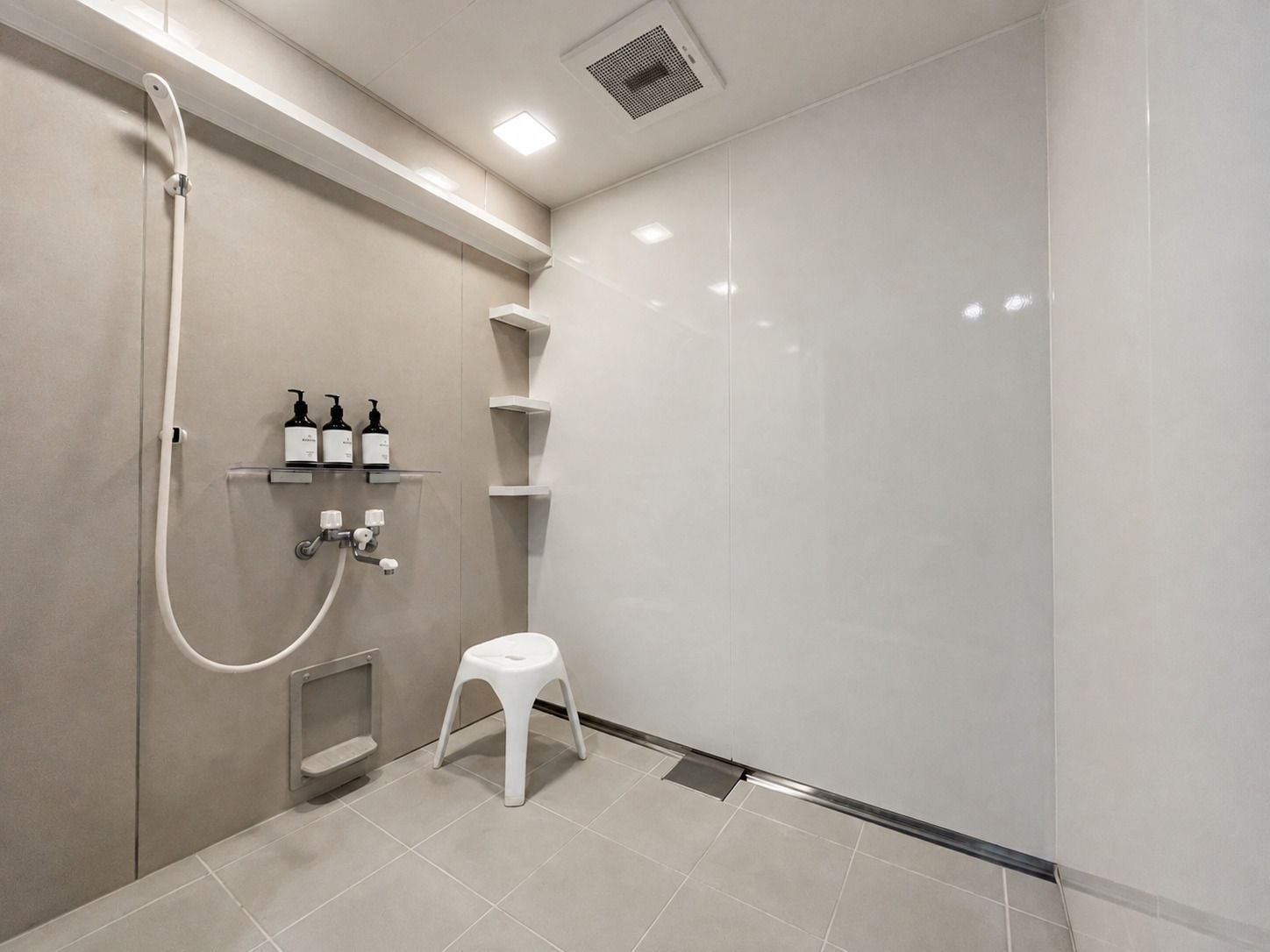 Un espace douche moderne doté d’un pommeau de douche à main, d’un tabouret et d’étagères de rangement.