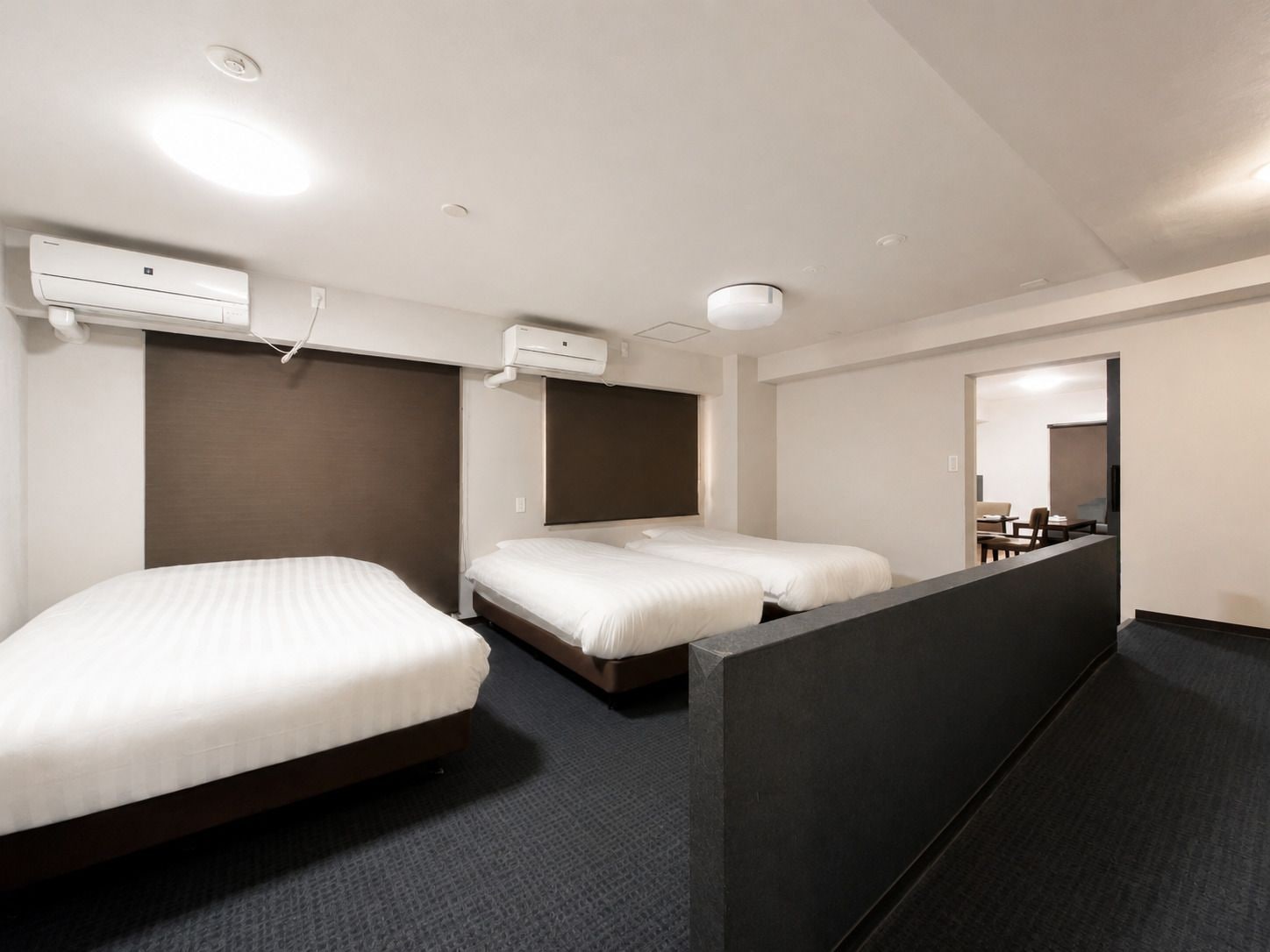 A hotel room with two beds, a dark partition wall, and a large mirror.