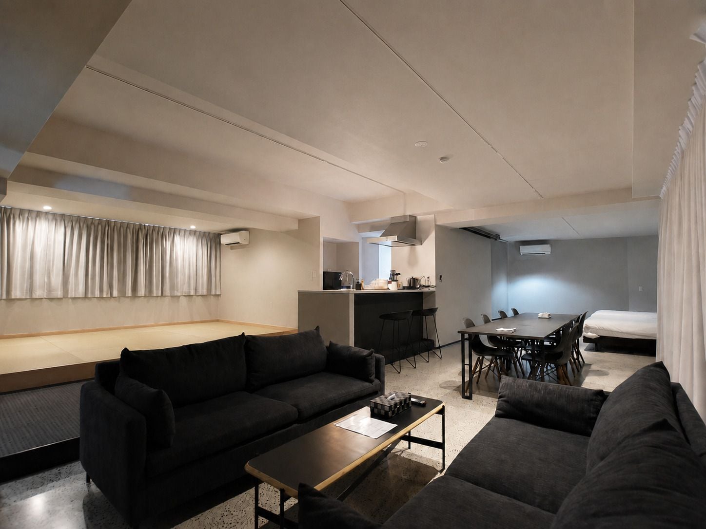 A modern living room with a sofa, coffee table, and a dining area with chairs and a table.