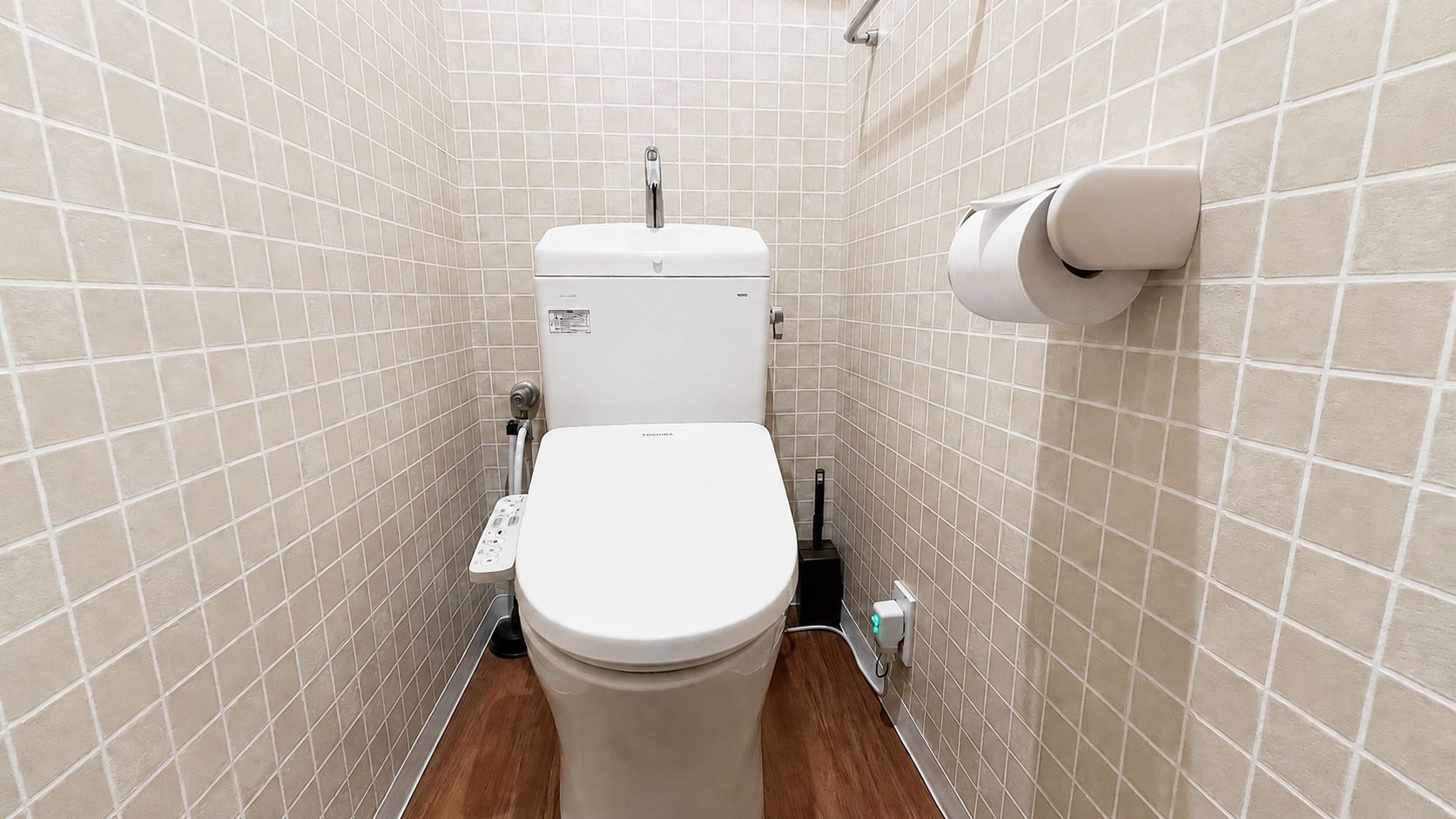 Een kleine betegelde badkamer met toilet, handdroger en papieren handdoekdispenser.