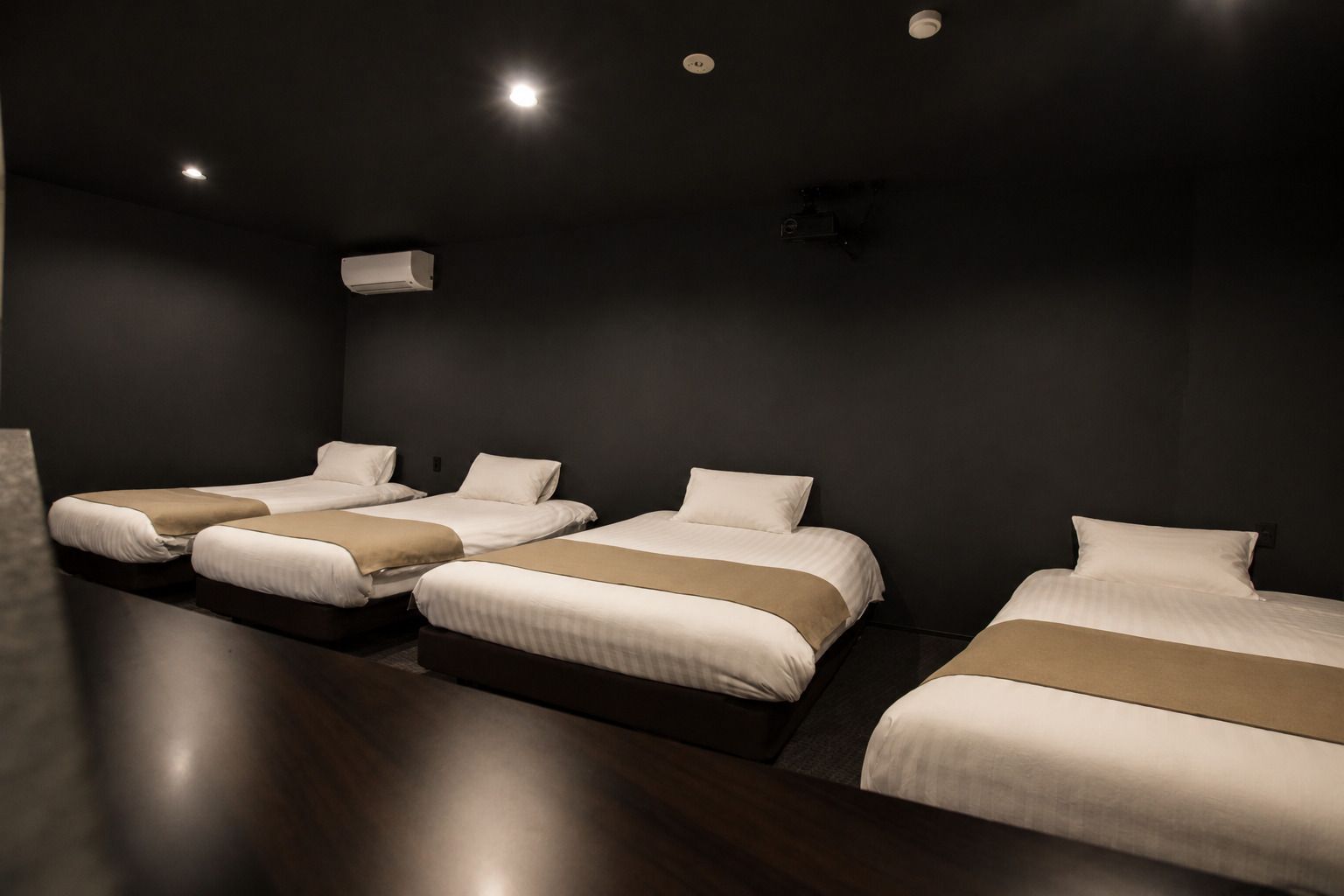 A hotel room with four single beds, a dark-colored wall, and a ceiling-mounted air conditioning unit.