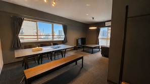 A conference room with a long table, chairs, a bench, a television, and a city view through large windows. - Randor Residence Tokyo Suites (Tokyo)