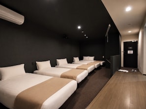 A hotel room with four beds aligned in a row, a dark wall, a wooden floor, and a door with a sign. - Randor Residence Tokyo Suites (Tokyo)