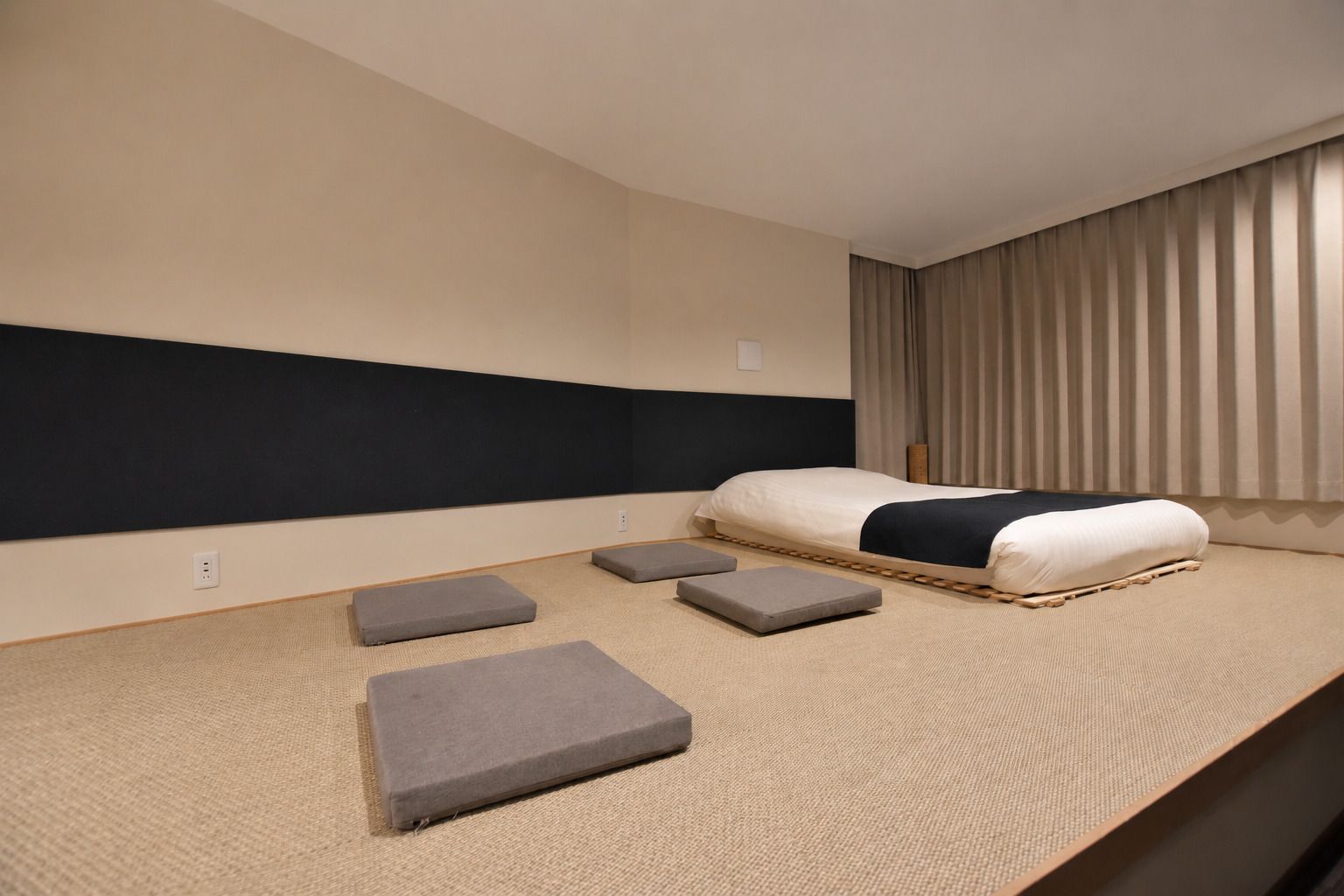 A hotel room with a bed, a headboard, a window with curtains, and a carpeted floor.
