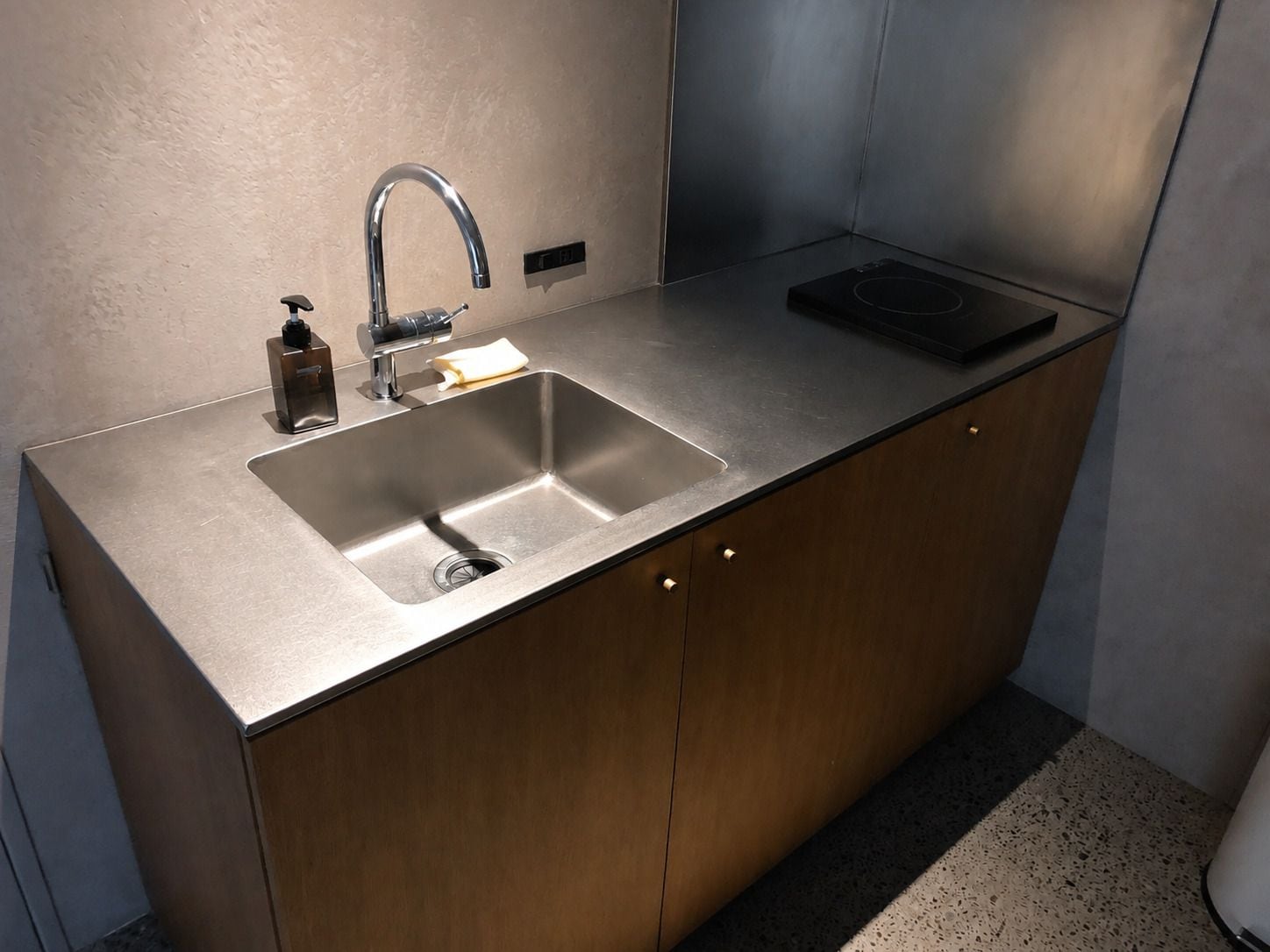A modern kitchen with a stainless steel sink, a faucet, a soap dispenser, and a built-in induction cooktop.