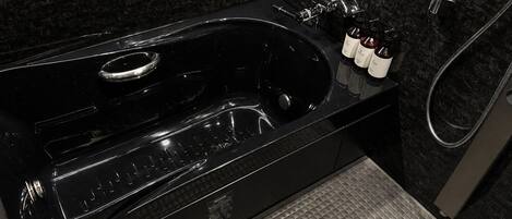 Una bañera negra con un cabezal de ducha manual, un panel de control y tres botellas de champú y acondicionador.