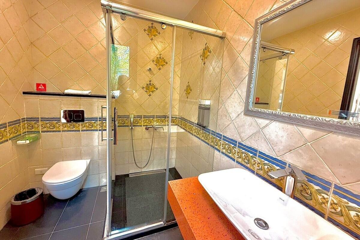 Un baño con ducha acristalada, inodoro blanco y lavabo con encimera roja.