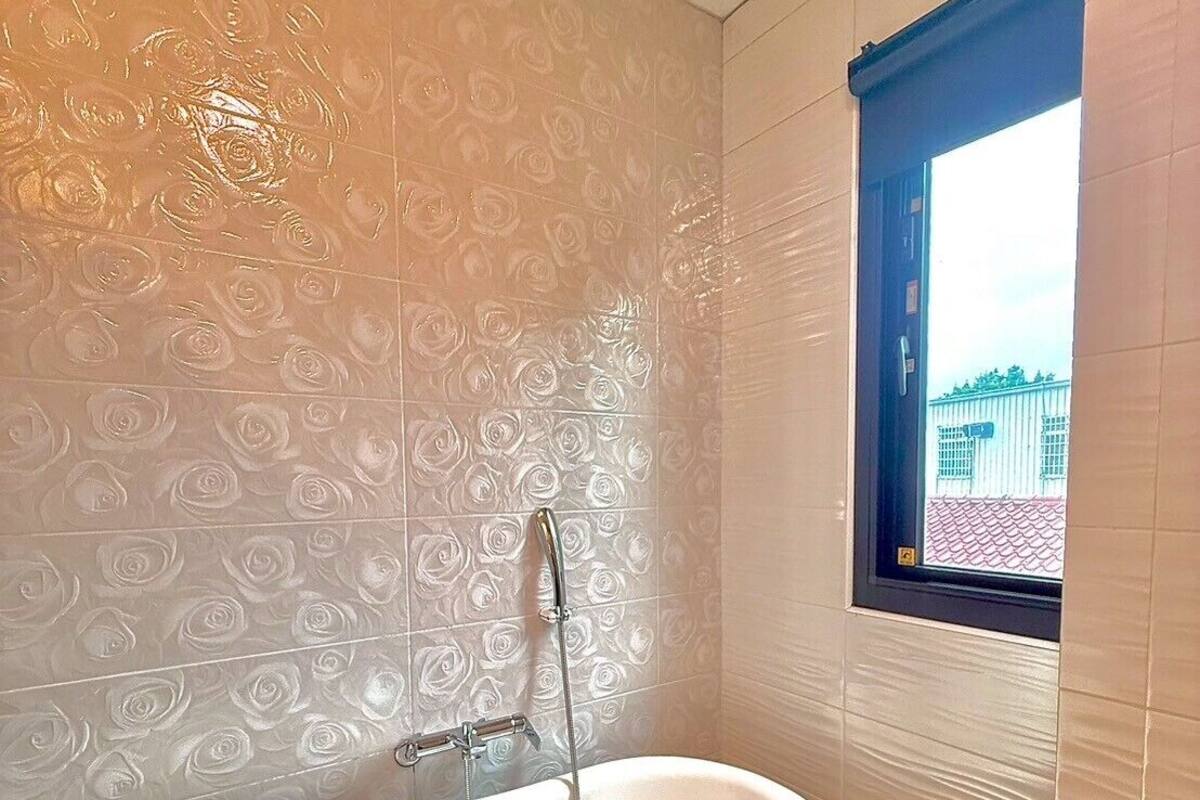 Un baño con una bañera independiente, un ventanal con vistas a un edificio y azulejos con diseños.
