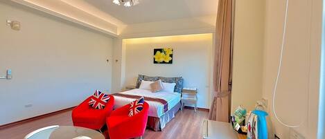 Una habitación de hotel moderna con una cama, dos sillones rojos, una mesa de centro de cristal, un escritorio con hervidor y una lámpara en el techo.